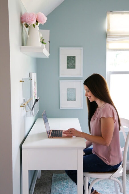 Woman in a pink shirt, sitting at a white desk, looking at Evernote on a laptop computer