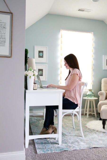 Woman in pink shirt sitting at a white desk, typing on a laptop computer