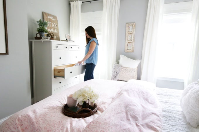 Woman putting away hand me down clothes in a white dresser in a bedroom