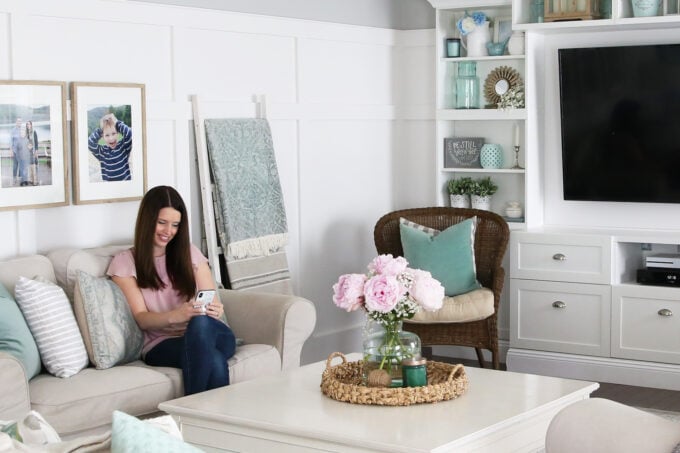 Woman in pink shirt sitting on a couch in a living room, looking at her phone