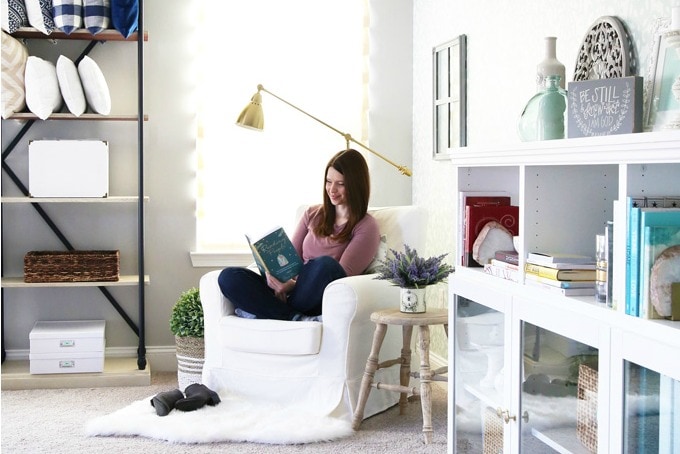 Woman reading a book in a white chair in the corner of a home office