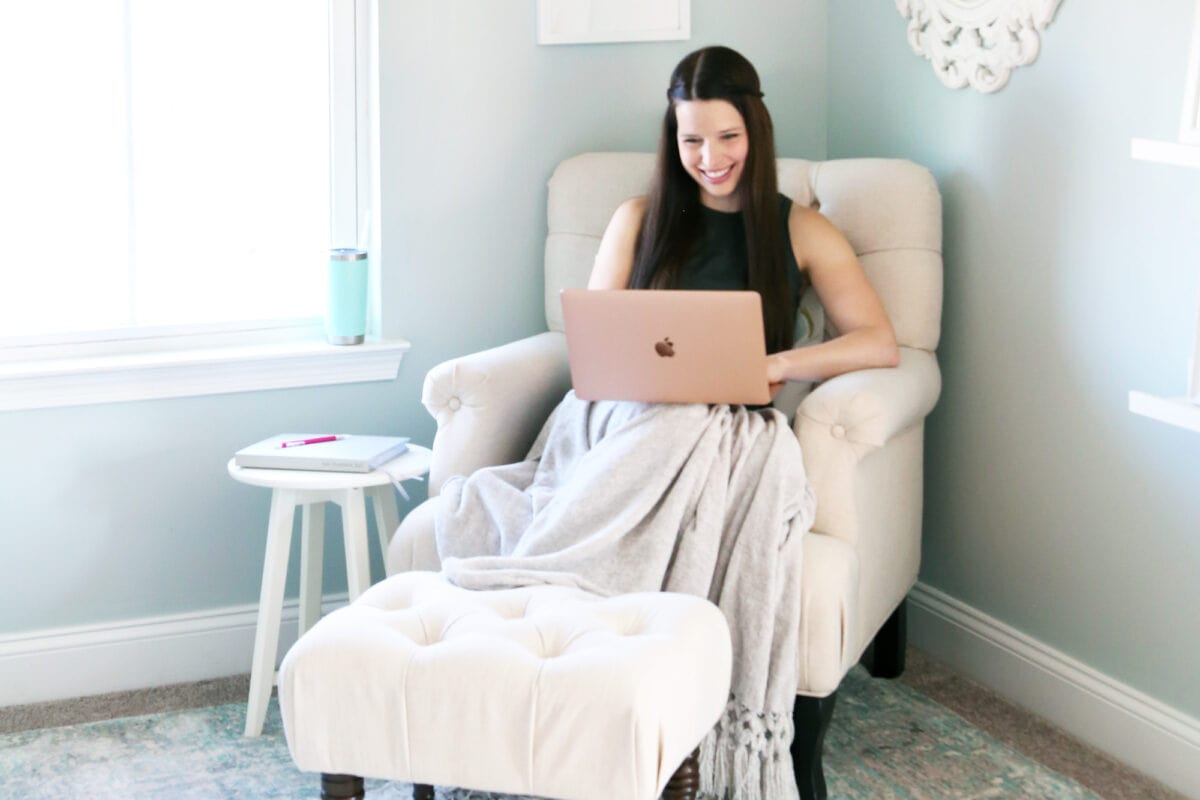 woman in a tan chair looking at a computer, updating sinking funds saving tracker spreadsheet