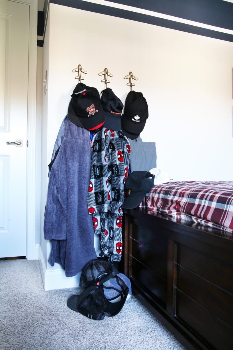 Messy hats on a bedroom floor and on cluttered hooks