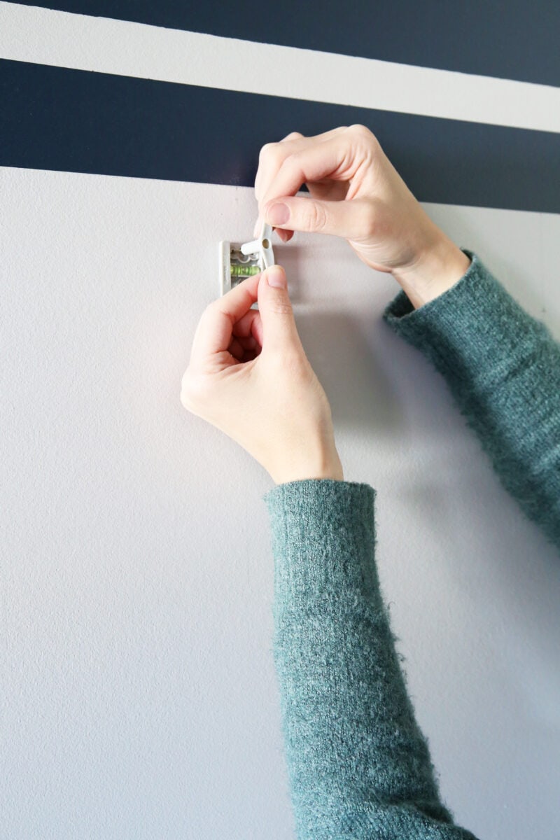 pushing a pin into the base plate of a j-hook to install an organized hat wall