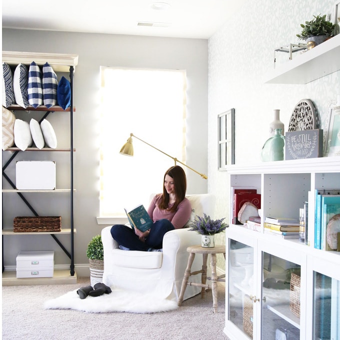 Woman reading a book, sitting in a white chair in a reading nook