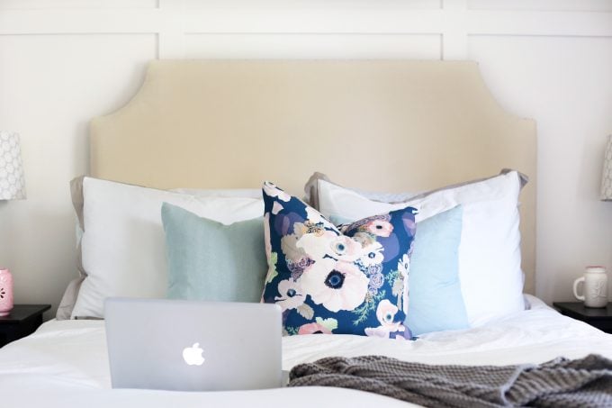 Laptop computer sitting on a bed with a white bedspread and blue floral pillow