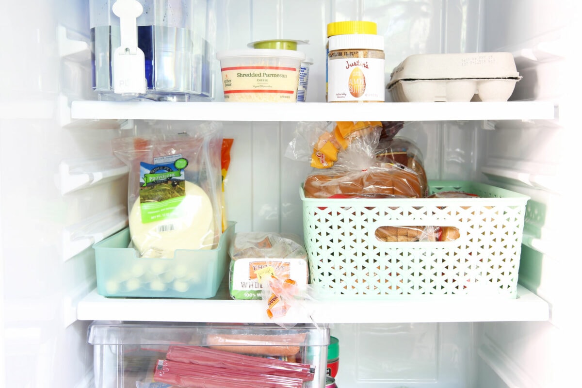 Shelves of an organized small refrigerator with aqua bins to corral various categories of food items