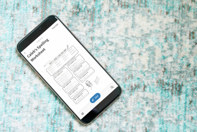 Scanned copy of a child's spelling worksheet in Evernote on an iPhone, sitting on an aqua and gray rug