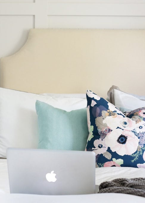 Laptop computer sitting on a bed with a floral pillow