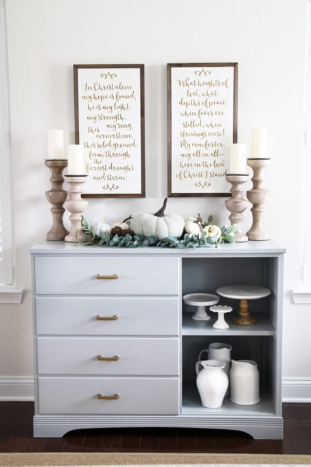 a gray styled sideboard with fall decor on top and pictures hanging on the wall