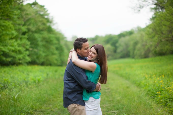 Husband kissing his wife on the cheek in the middle of a field