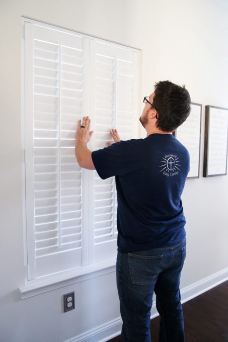 Donnie holding a wooden shutter up to the window to make sure it fits