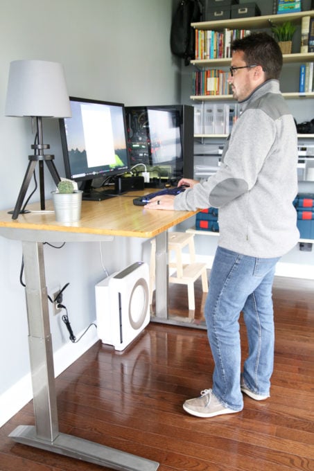 A man at a standing desk looking at a desktop computer