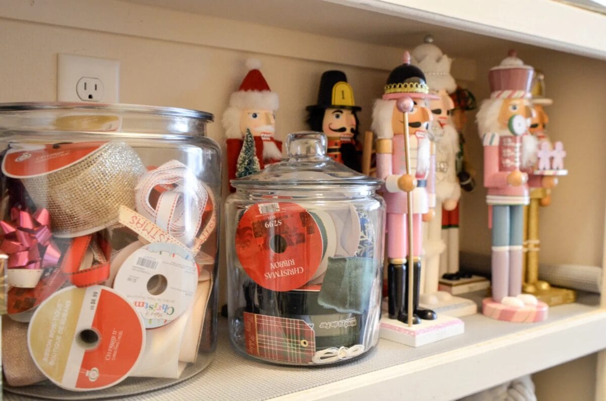 Shelves display glass jars filled with ribbons and crafting materials. Alongside, an array of colorful nutcracker figurines stand in a row, adding a festive touch to the scene. These Christmas decoration storage ideas bring both organization and holiday spirit to any space.