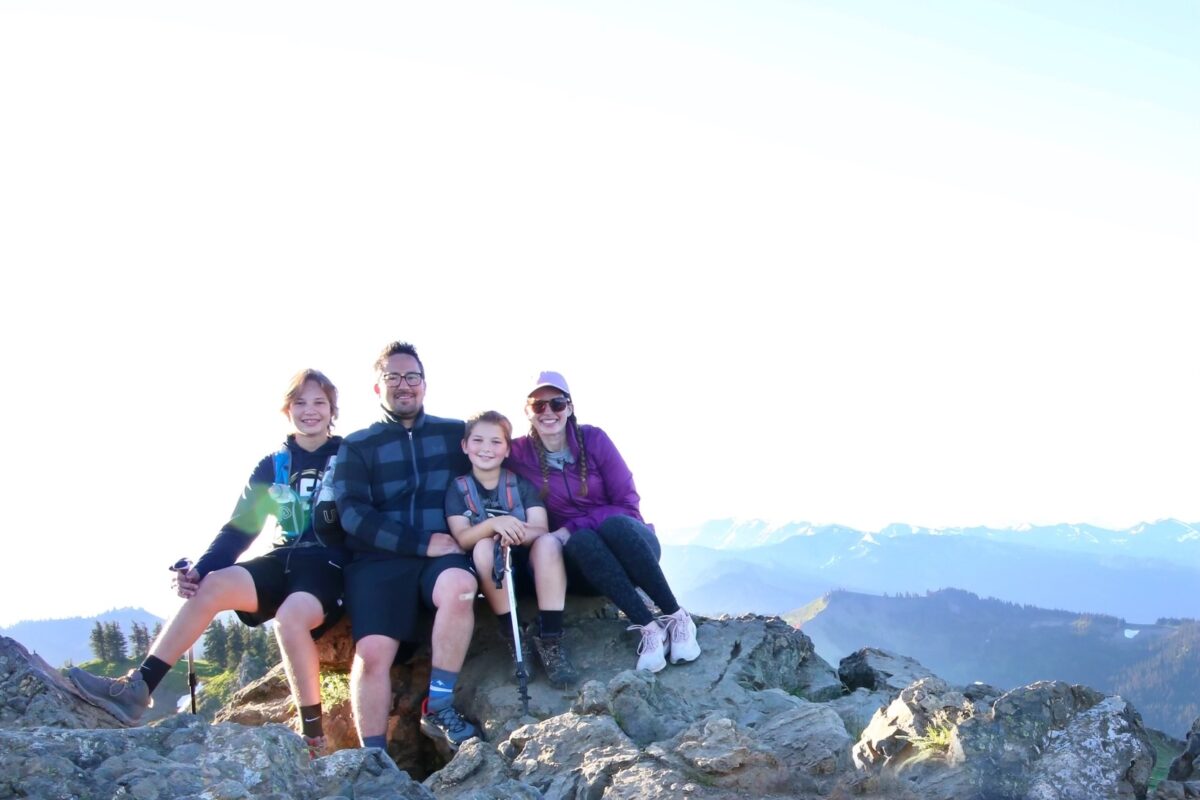 A dad, mom, and two sons sitting on rocks in Olympic National Park