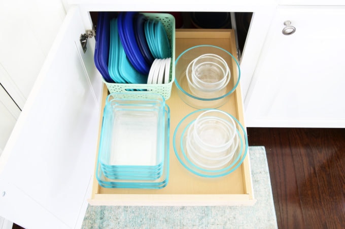 top view of food storage containers on a pull out shelf with a basket full of lids