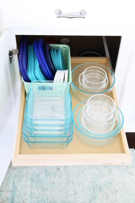 all of the food storage containers stacked nicely on a pull out shelf next to the lids in a basket