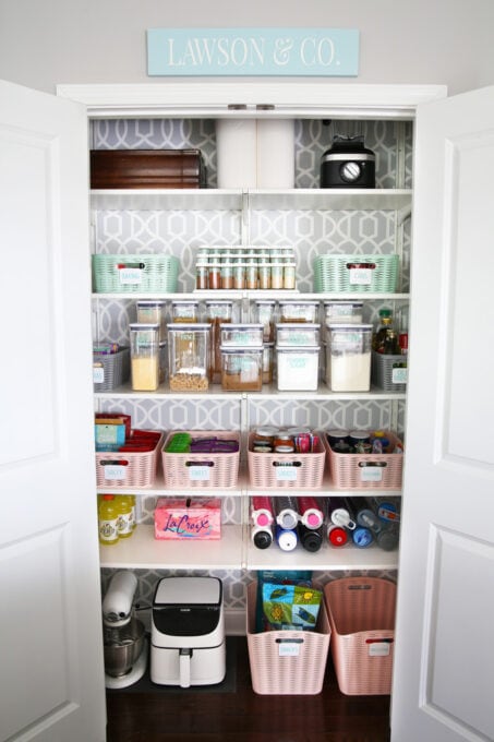 organized pantry with decanted dry goods and colorful bins holding snacks, baking items, and canned goods