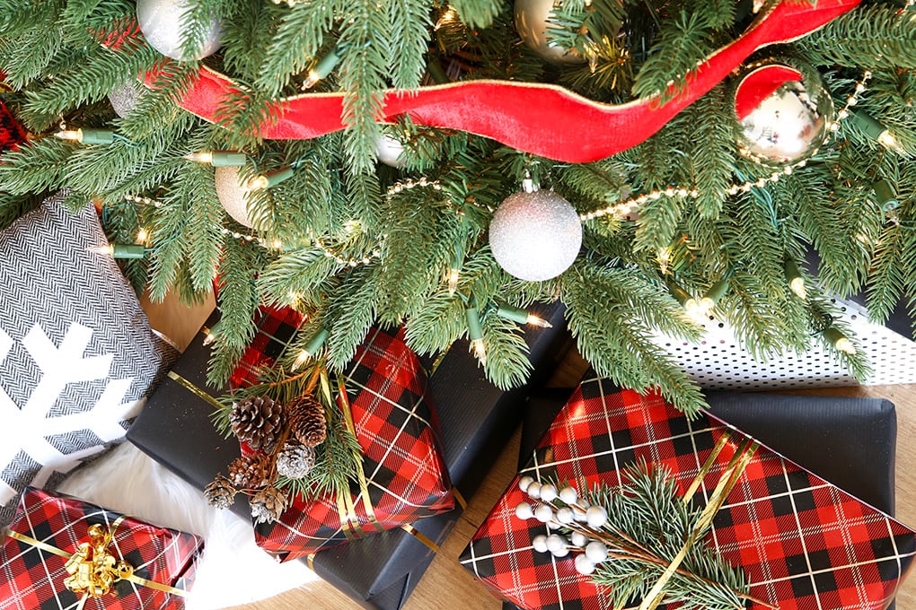 Gifts under a Christmas tree wrapped in coordinating wrapping paper with fresh pine twig toppers