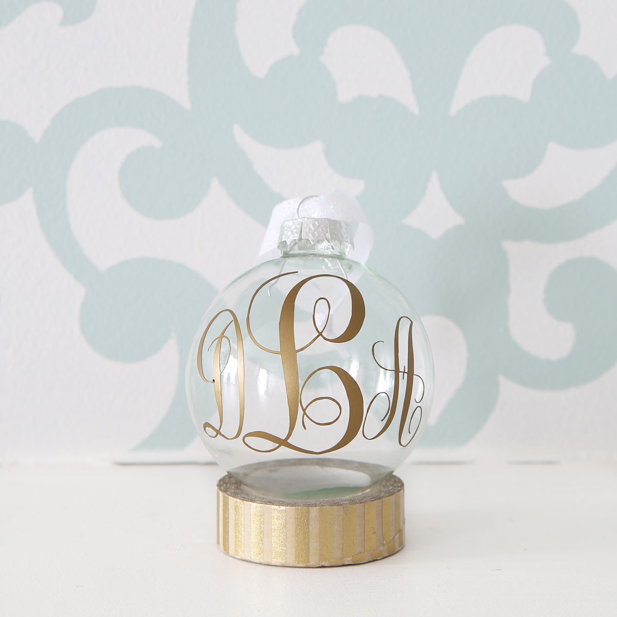 Gold Monogrammed Christmas Ornament in Front of an Aqua Stenciled Wall