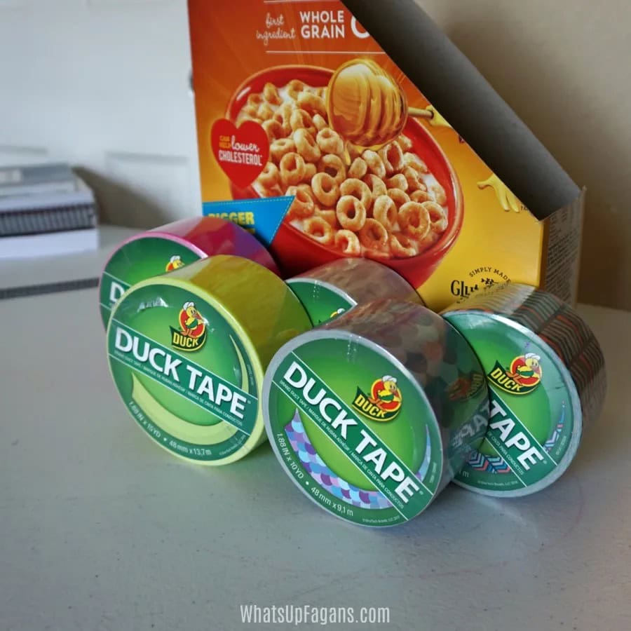 Cut cereal box with duck tape lined up in front to be used as supplies for a DIY magazine holder.