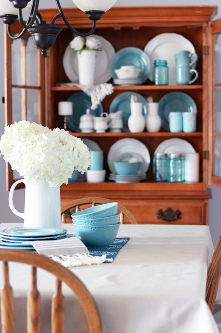 a hutch with white and blue dishes behind the dining table