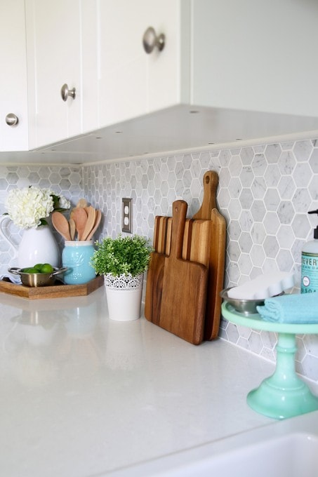 Kitchen accessories, cutting boards, Carra marble backsplash. Beautiful white IKEA SEKTION GRIMSLOV kitchen with aqua and green accents, a gorgeous marble hexagon backsplash, and quartz countertops. | JustAGirlAndHerBlog.com