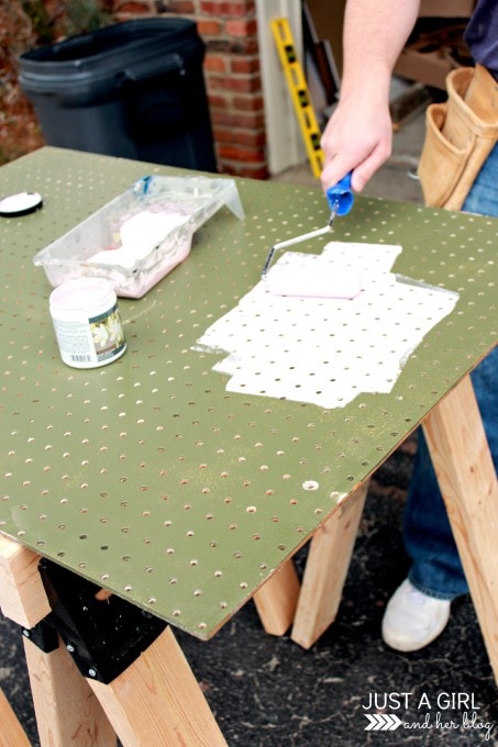 using a small foam paint roller to paint a green pegboard Behr Rosy Lavender