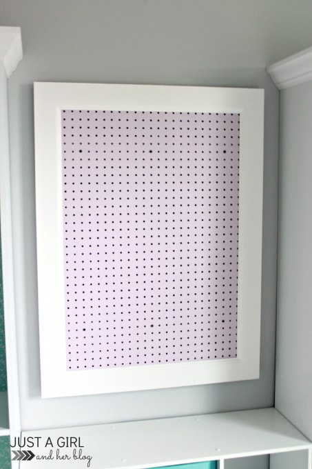 empty lavender pegboard with a white frame hung on the wall in an organized craft room / home office