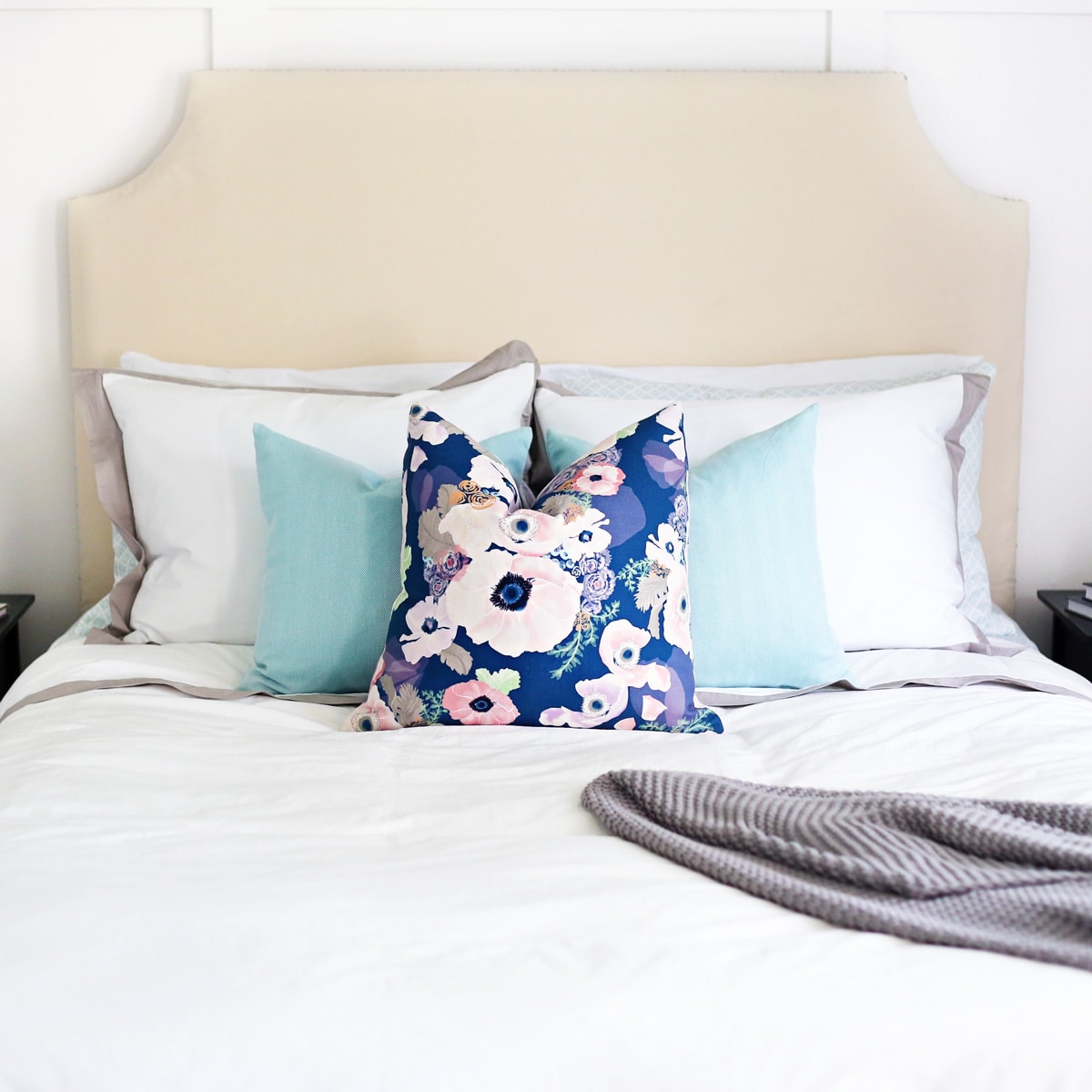 Upholstered headboard in a primary bedroom with a white bedspread and blue and pink floral pillow