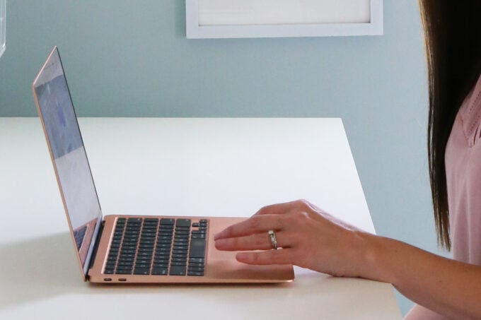 A woman's hand operating a laptop computer, which is sitting on a white desk