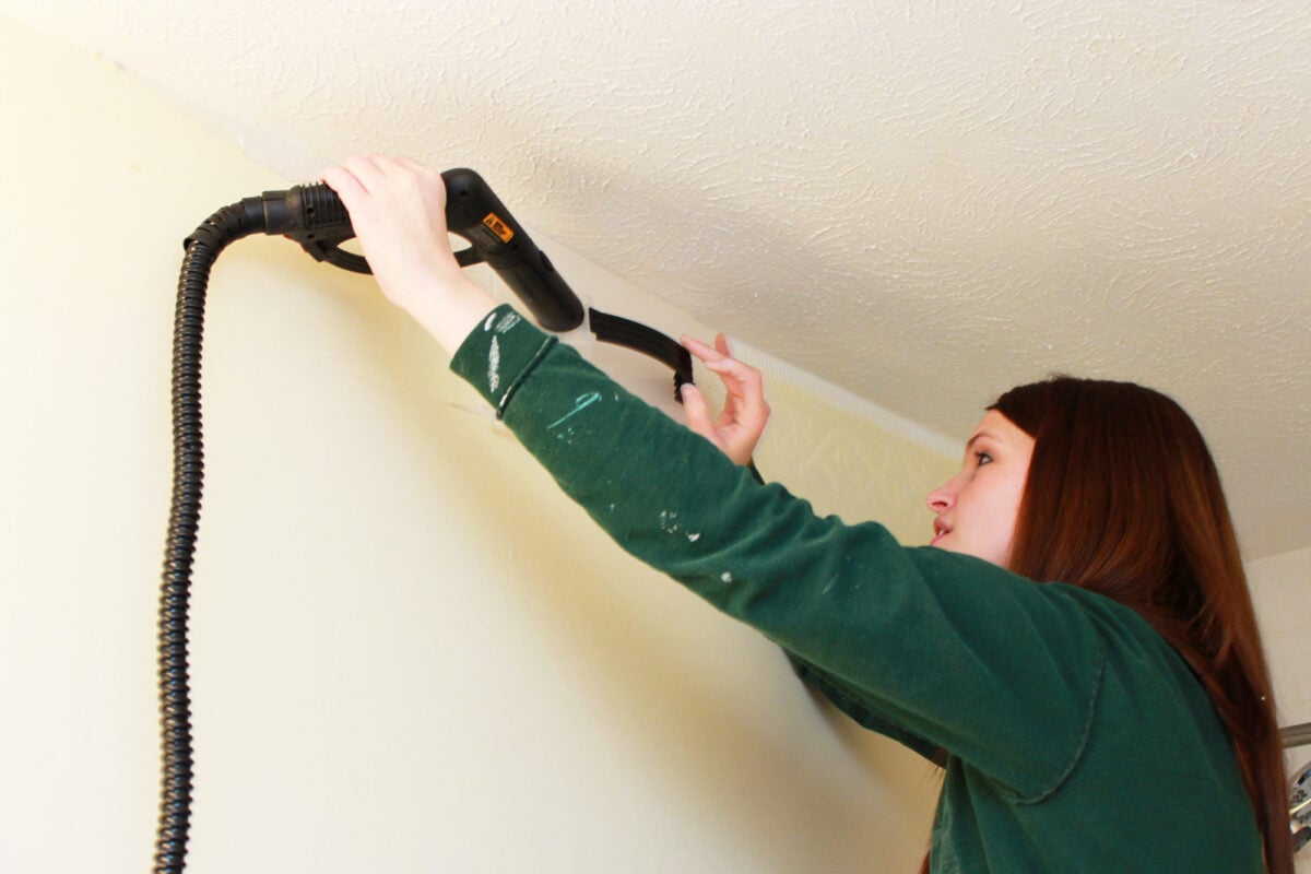 Woman removing a wallpaper border with a steam machine