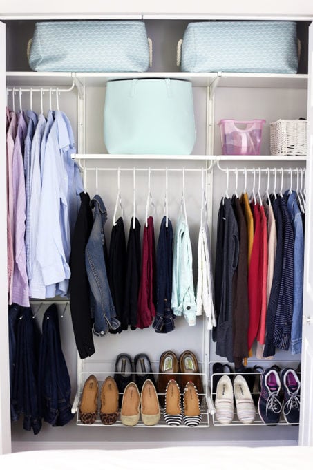 organized closet with light blue bins, items hanging on white hangers, and organized shoes lined up in a row