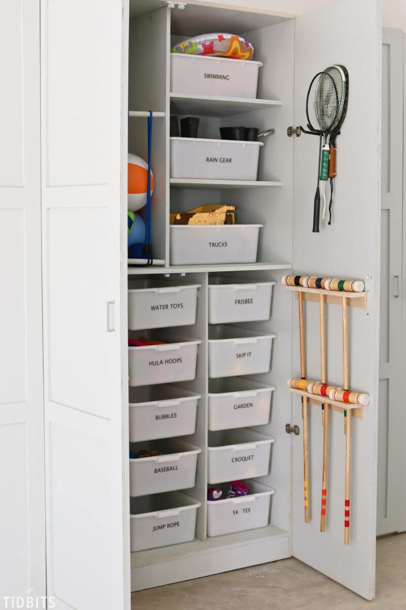 White cabinet with bins inside storing outdoor toys