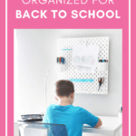 Boy in a blue shirt sitting at a white desk doing homework with an organized peg board for back to school